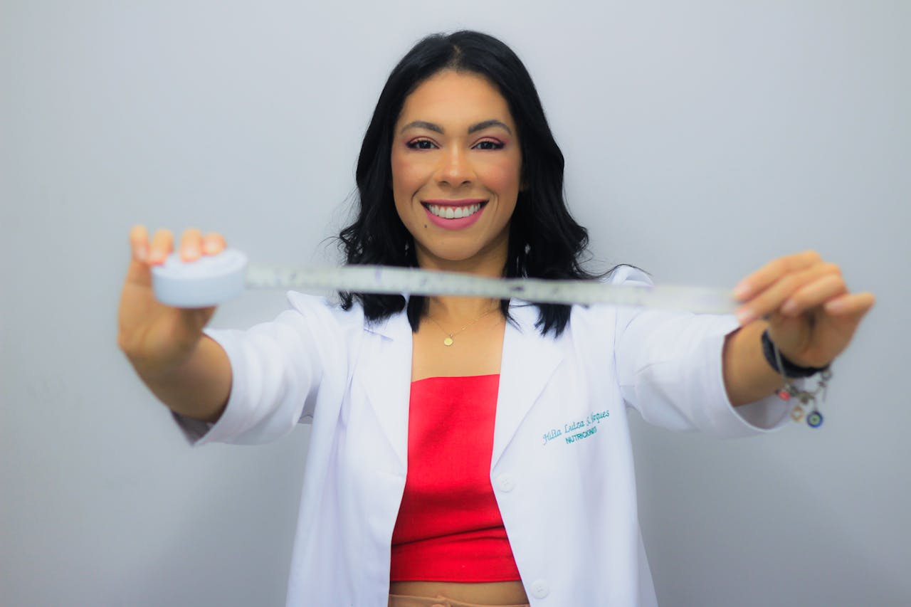 Cheerful nutritionist smiling broadly while holding a measuring tape, symbolizing healthy lifestyle and wellness.